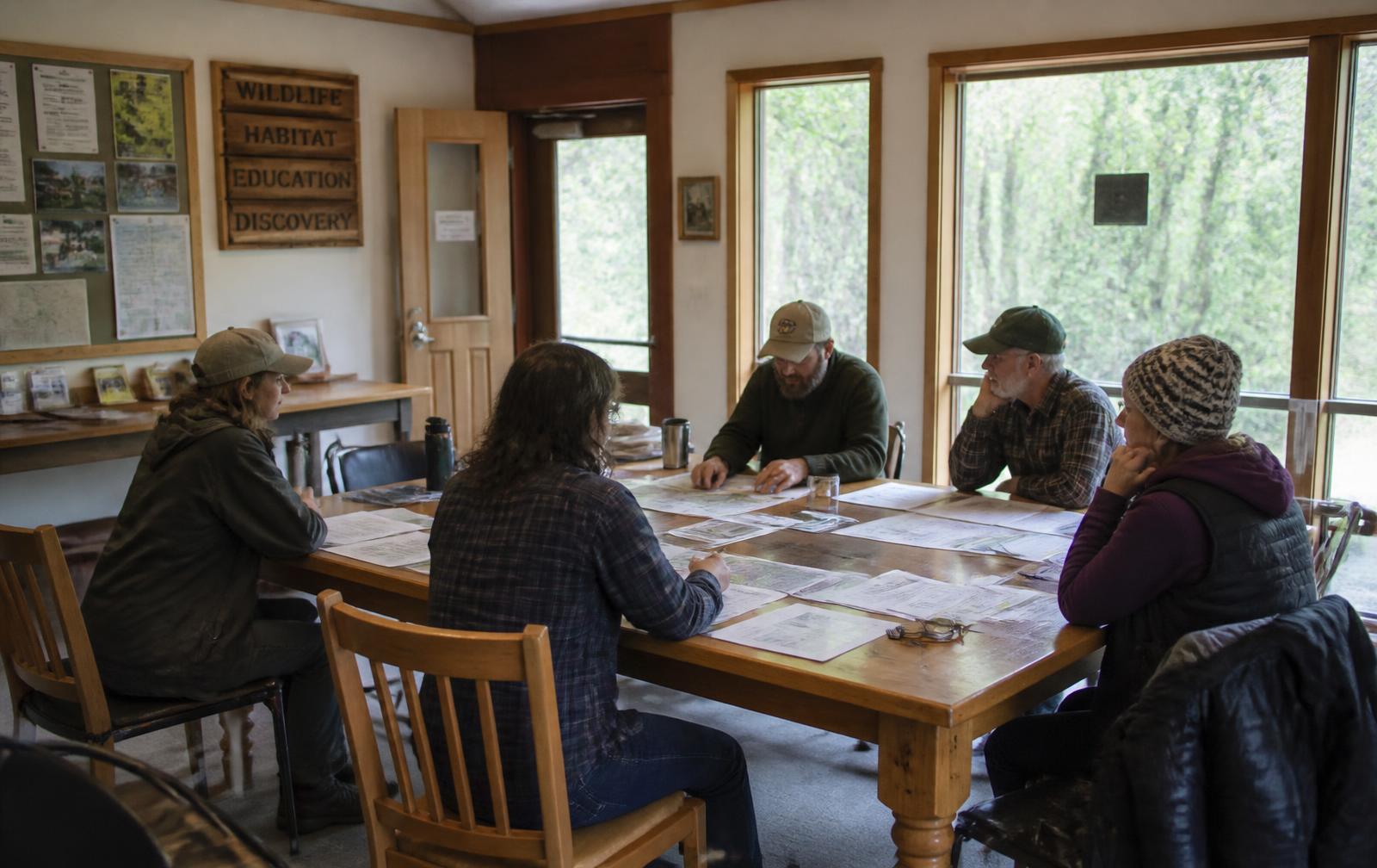 Staff and trustees reviewing printed plans and maps around a table in a nature center meeting room.